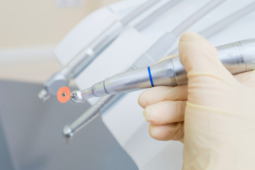 Closeup shoot of doctor hand holding dental instruments in clinic, turbines, handpieces and drills at background.