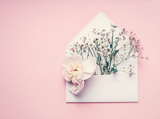 Opened envelop with flowers arrangement on pastel pink background, top view, copy space. Creative...