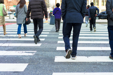 People are walking on a crosswalk on a city street.