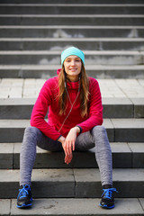 Urban style,smiling athletic sport woman sitting in headphones on the steps,bright