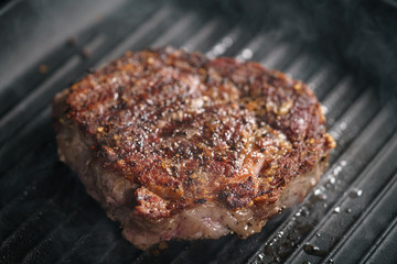 beef rib eye steak on grill pan closeup, shallow focus