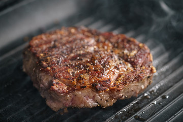 beef rib eye steak on grill pan closeup, shallow focus