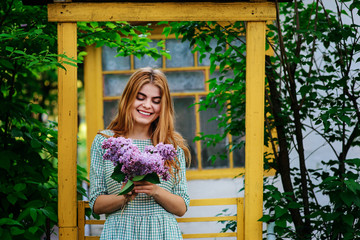 Beautiful young woman with bouquet of lilac in spring garden.