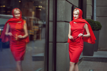 Stylish woman looks at the shop window, she is fashionable in scarlet dress.