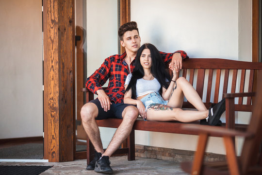 Two hipster models young man and woman with tattoo sitting on the bench with a wistful smile, looking into the distance. Beautiful young couple during a romantic date, urban style