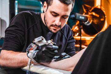master tattooist makes a tattoo on the skin of the hand client girl in a workshop with special...