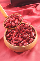 red kidney beans in wooden bowl and wooden spoon on red background