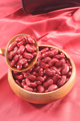 red kidney beans in wooden bowl and wooden spoon on red background