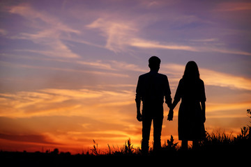 Fototapeta na wymiar young couple is holding hands on a background sunset silhouette