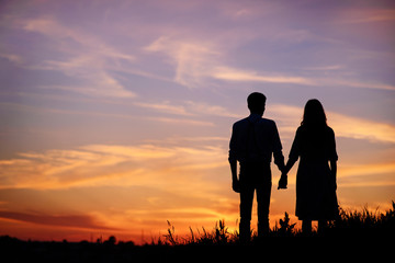 Fototapeta na wymiar young couple is holding hands on a background sunset silhouette