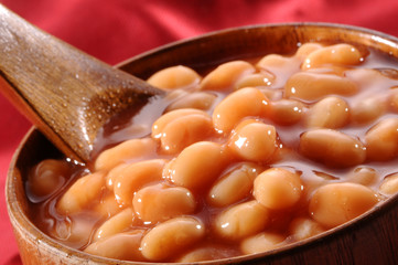 baked beans with gravy in wooden bowl and wooden spoon on red background