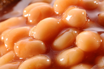 baked beans with gravy in wooden bowl and wooden spoon on red background