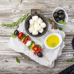 Healthy snack: mouth-watering kebabs on a picnic with tomatoes, mozzarella, salami, black olives, Basil, tortellini pasta on a cutting Board on wooden background with olive oil and herbs. From the top