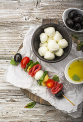 Healthy snack: mouth-watering kebabs on a picnic with tomatoes, mozzarella, salami, black olives, Basil, tortellini pasta on a cutting Board on wooden background with olive oil and herbs. From the top