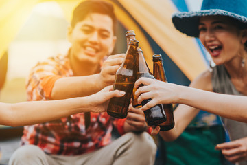 Friends laugh and smile sitting outside their tent toasting with beers