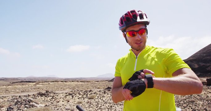 Mountain biking man using smartwatch sport watch looking at heart rate monitor fitness tracker resting during MTB bike ride in nature. Male cyclist wearing sunglasses and cycling helmet. RED EPIC.