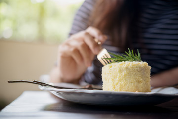A woman's hand cutting cheese cake with fork in coffee shop