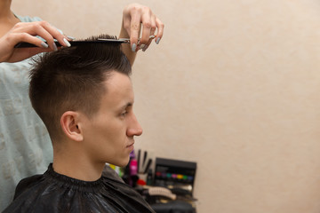 Fototapeta premium Side view of young man getting groomed at hairdresser while sitting in chair at barbershop.