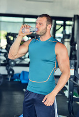 Resting time. Handsome young men in sports wear wearing towel on his shoulders and holding water bottle while sitting at gym