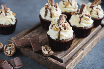 Homemade chocolate  cupcake with nuts and vanilla frosting on wooden board and dark stone background, selective focus. Delicious dessert  for birthday, festive seasons,  engagement or valentine day