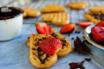 Belgian waffles in the shape of hearts with fresh strawberries and chocolate topping on blue table. Homemade healthy breakfast, selective focus