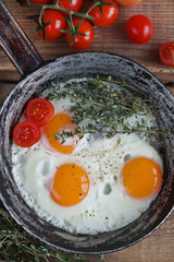 Fried eggs in a frying pan with herbs, cherry tomatoes, bread, olive oil and spices on rustic wooden background. Healthy breakfast, top view