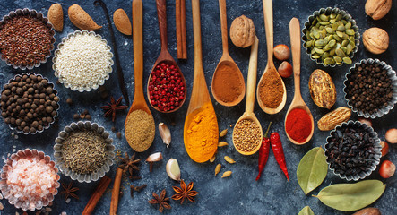 Various indian spices in wooden spoons and metal bowls, herbs and nuts on dark stone table....