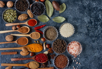 Various indian spices in wooden spoons and metal bowls, herbs and nuts on dark stone table. Colorful spices, top view,space for text. Healthy food background