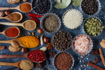 Various indian spices in wooden spoons and metal bowls, herbs and nuts on dark stone table. Colorful spices, top view. Healthy food background