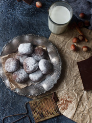 Homemade chocolate crinkles in powdered sugar on vintage plate and a glass of milk on dark stone...