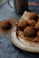 Homemade chocolate truffle candies with cocoa powder on vintage plate and dark stone background. Sweet dessert, selective focus