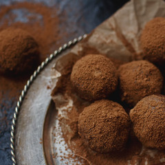 Homemade chocolate truffle candies with cocoa powder on vintage plate and dark stone background. Sweet dessert, selective focus
