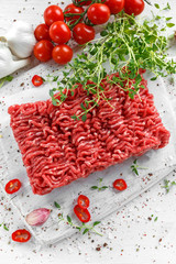 Fresh Raw Beef Minced Meat with salt, pepper, chilli and fresh thyme on white board.