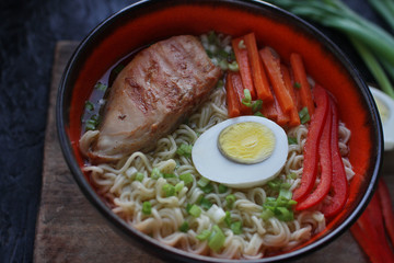 Ceramic bowl of traditional asian ramen soup with noodles, spring onion, chicken, sliced egg on dark stone table. Top view, selective focus.