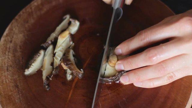 Close up of female hands cutting previously soaked shiitake mushrooms on round wooden board. Shiitake is a famous ingredient for miso soup (japanese traditional dish). Table top view.