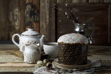 Easter cake with quail eggs and white craft tea set and vase with willow on brown wooden background with space for text. Easter holidays. Still life