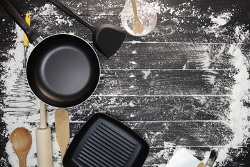 Cooking background with pans, flour, rolling pin,eggs,wooden spoons on black wooden background,cooking concept top view.