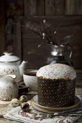 Easter cake with quail eggs and white craft tea set and vase with willow on brown wooden background with space for text. Easter holidays. Still life