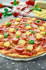 Fresh baked pizza hawaii with ham and pineapple, basil, tomatoes on backed paper