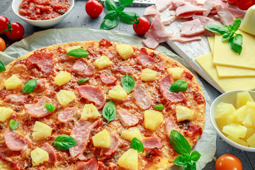 Fresh baked pizza hawaii with ham and pineapple, basil, tomatoes on backed paper