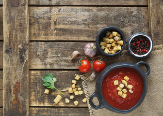 tomato soup with fresh herbs, clove, black pepper and crackers on rustic wooden background, top view.