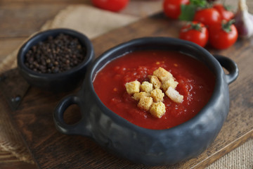 tomato soup with fresh herbs, clove, black pepper and crackers on rustic wooden background,  selective focus