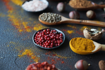 Various indian spices in wooden spoons and metal bowls, herbs and nuts on dark stone table. Colorful spices, selective focus. Healthy food background