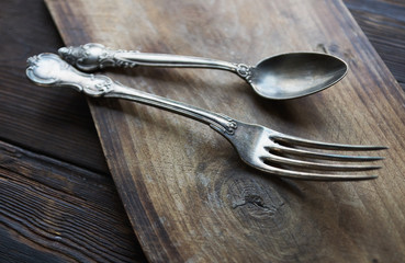 Vintage kitchen cutlery - spoon and fork on  dark cloth and rustic wooden background, selective focus