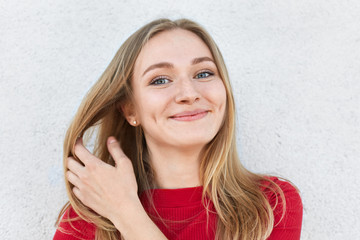 Pleased woman with blonde hair, luminous eyes and gentle smile having dimples on cheeks touching...