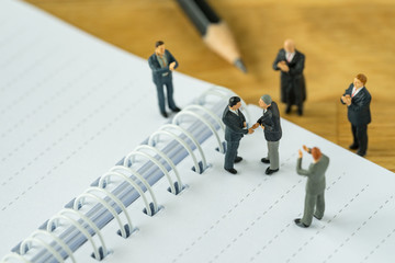Miniature people: Small figure businessmen handshaking and others clapping on notebook and pencil as business agreement concept
