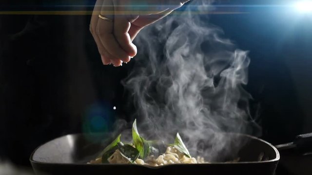 A chef pours salt on the Chinese noodles in the pan .Slow motion.
