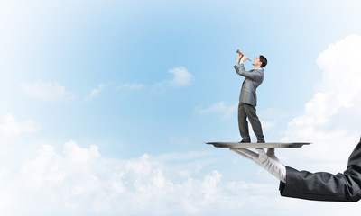 Businessman on metal tray playing fife against blue sky background