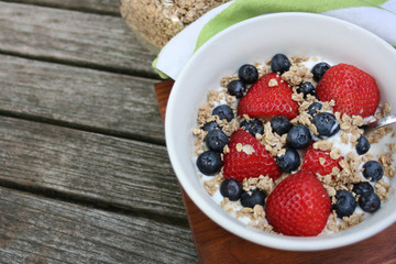 Healthy breakfast bowl. Granola in white bowl with greek yogurt and berries on wooden background