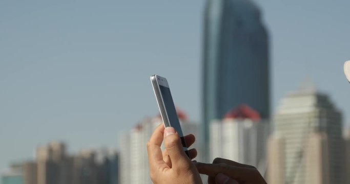 4k A girl using a smartphone aganist the modern business building background.